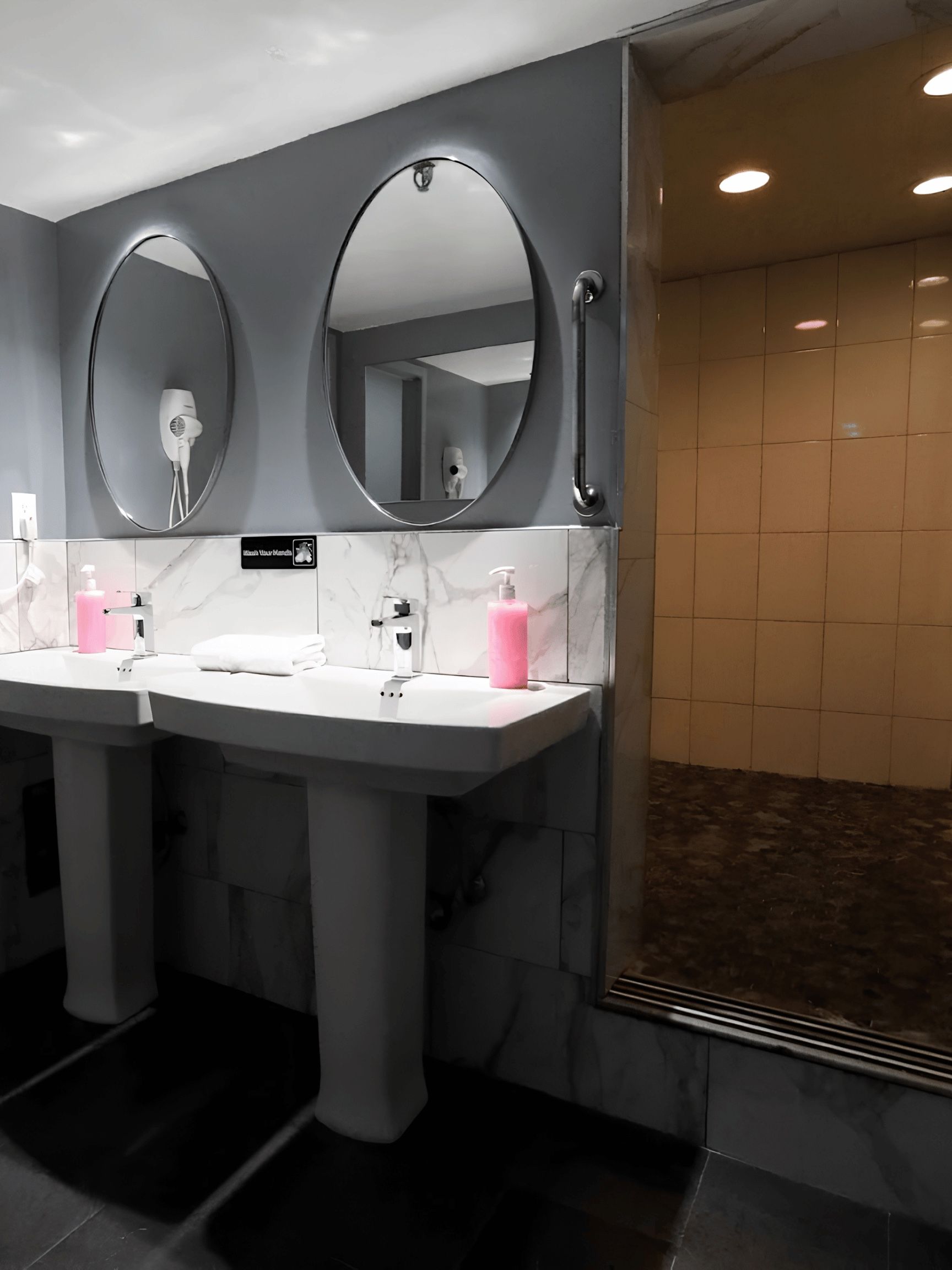 Washroom with two pedestal sinks and round mirrors beside a tiled walk-in shower